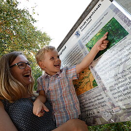 Mutter mit Kind an Informationstafel des Biotoplehrfpades Ingolstadt