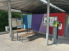 Unter dem Dach am Großparkplatz steht eine Radreparaturstation mit der man die nötigsten Reparaturen an seinem Fahrrad vornehmen kann. Links ist ein Tisch und zwei Bänke für eine kleine Rast.