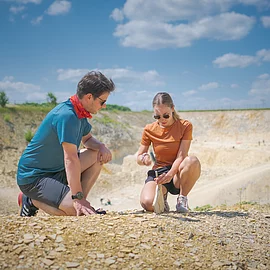 Ein Mann im blauen Shirt kniet neben einer Frau, die mit Hammer und Meißel vorsichtig eine Steinplatte im Fossiliensteinbruch Blumenberg teilt.
