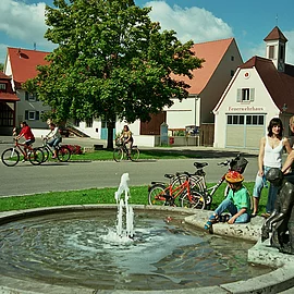 Radler legen eine kleine Rast am Brunnen in der Ortsmitte von Muhr am Altmühlsee ein.