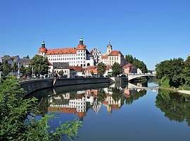 Stadtansicht mit Schloss und Brücke, Spiegelung im Fluss, blauer Himmel, Bäume am Ufer