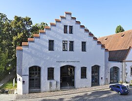 Gebäude mit Treppengiebel und Schriftzug Tourist-Information, davor gepflasterte Straße und blauer Pkw.