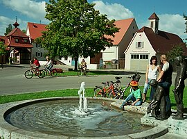 Radler legen eine kleine Rast am Brunnen in der Ortsmitte von Muhr am Altmühlsee ein.